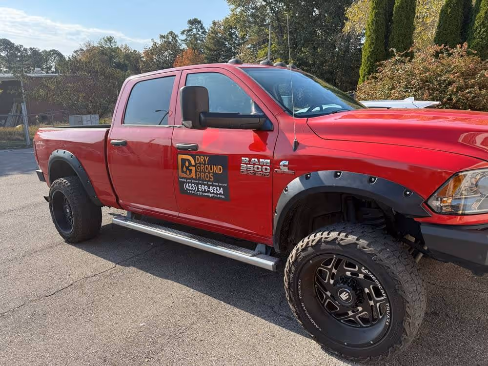Red RAM 3500 pickup truck with Dry Ground Pros logo and contact information on the driver door parked on a paved surface.