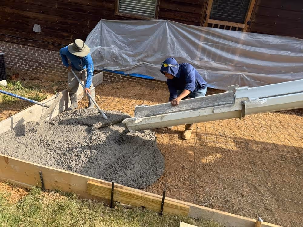 Two workers spreading poured concrete inside a wooden frame for a construction project outdoors.